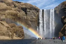 A group of people standing at the base of a waterfall with a rainbow over them.