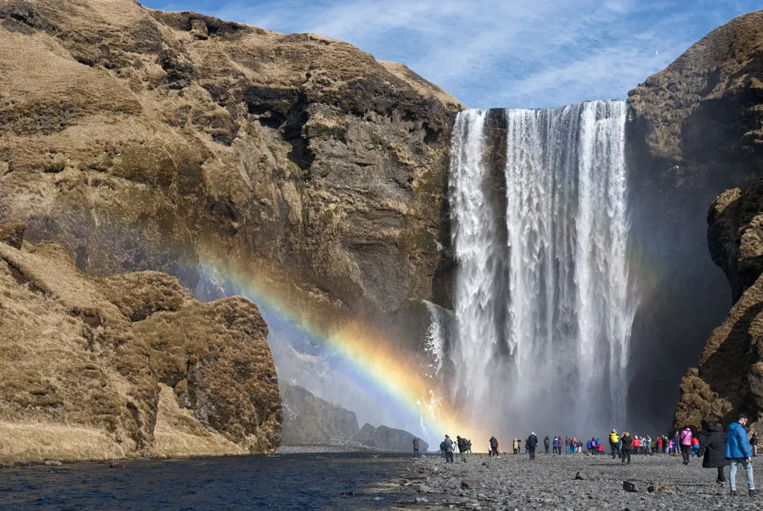 A group of people standing at the base of a waterfall with a rainbow over them.